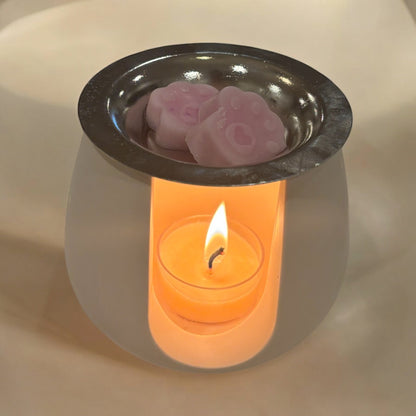 White paw-print wax melt burner made from eco-friendly jesmonite, featuring a lit tealight and melting wax, creating a cozy and aromatic atmosphere